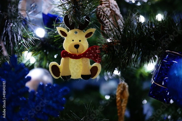 Obraz Cute Christmas decoration in a shape of a little white reindeer with a scarf, hanging on a Christmas tree