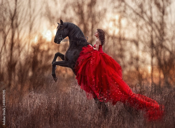 Obraz Beautiful curly-haired girl in a red dress riding a horse on its hind legs