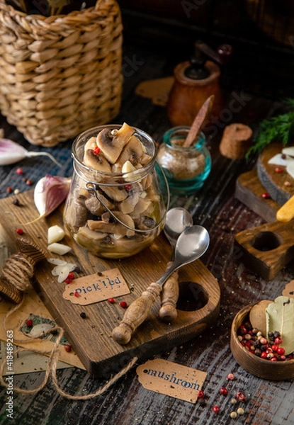 Fototapeta homemade marinated mushrooms in glass jar on wooden board with herbs, dill. pepper, vintage spoons
