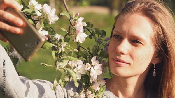 Obraz A beautiful young girl makes a selfie on the background of flowering trees. Photo for social networks and instangram