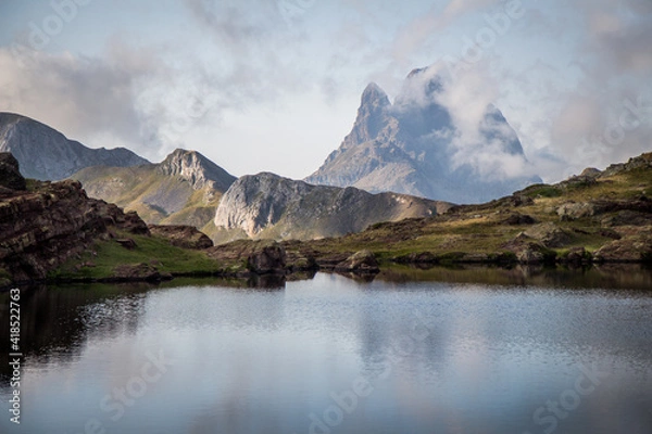 Obraz Stunning view of a beautiful mountain surrounded by clouds in the Pyrenees with a quiet lake in the foreground
