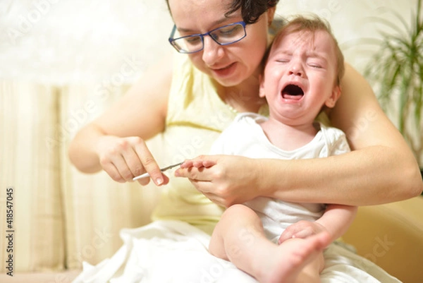 Obraz selective focus The mother cuts the child's toenails on the arm with baby safe scissors. Self care authentic concept. Mother care is most important for baby healthy life lifestyle. The baby is crying
