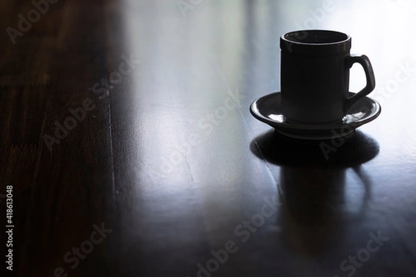 Obraz Cup of coffee with saucer on wood table. Figure in shadows. Reflection on table