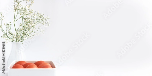Obraz Easter eggs in a white square dish, on a white table, and a vase with delicate white flowers. Banner, space for text