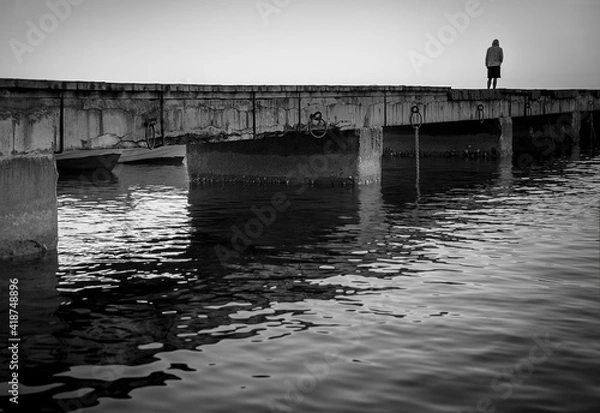 Fototapeta Sorrow. Silhouette of a lonely man on a pier, black and white image.