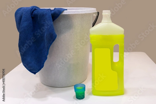 Fototapeta a bucket with a rag and an open bottle of detergent on a white table