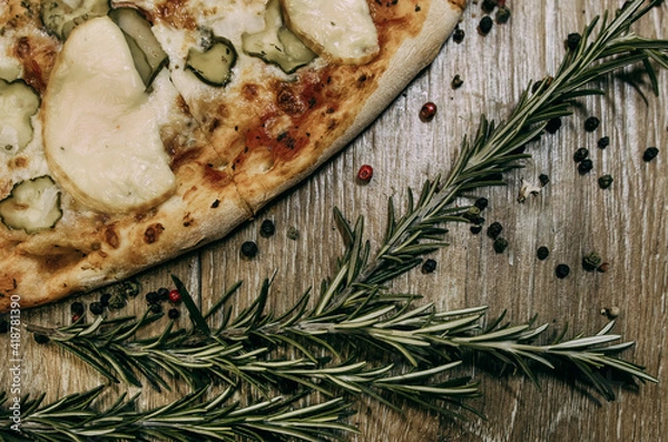 Fototapeta Super cheesy pizza with hunting sausages, pickles and melted cheese. sprigs of rosemary lie nearby