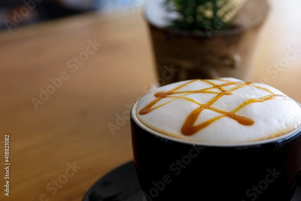 Fototapeta Close up hot cappuccino, latte, caramel macchiato on table with blur coffee shop background. Process with warm vintage tone style.