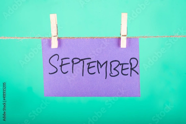 Fototapeta  September word written on a Purple color sticky note hanging with a wire in a Cyan background.