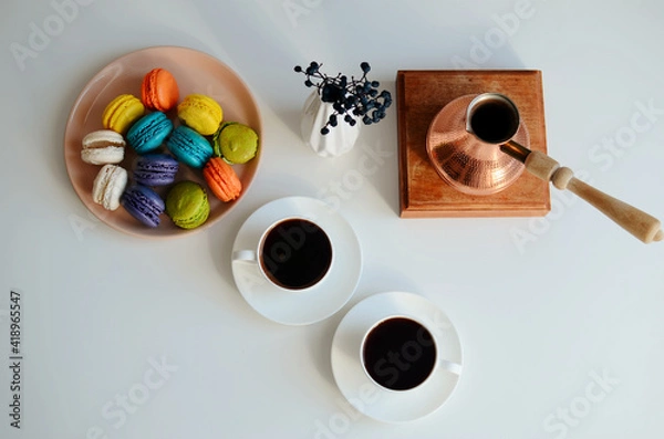 Fototapeta Two cup of coffee, multicolored macaroons, turkish coffee pot on white background, top view