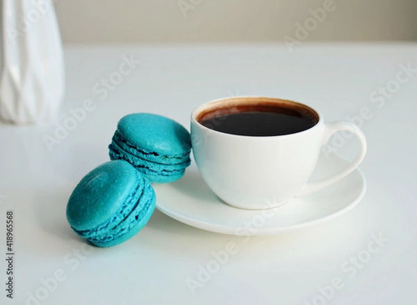 Fototapeta White cup of coffee, multicolored macaroons on white background, close up