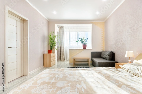 Fototapeta Simple cheap interior of light bedroom with loggia, sofa, and indoor plants. Rostov-on-Don, Russia - 10 november 2020