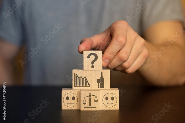 Obraz Business and finance concept. Hand holds wooden wooden blocks with finance icons and business. securities, student hat, 
books, time, home, car, family, question, target, gears,  securities, money, id