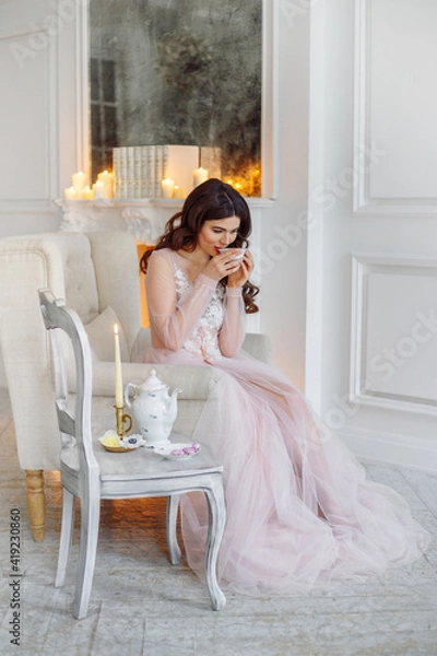 Obraz Morning of the bride. She is in a white interior drinking tea. The room has a classic white fireplace