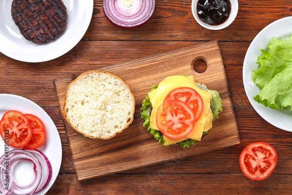 Obraz Homemade hamburger with cutlet, salad, onion, tomato and cheese. Cheeseburger, burger. Step by step. Top view. Cooking a burger