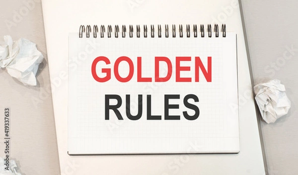 Fototapeta The word golden rules is written in a notebook that sits on a gray desktop along with a laptop. Business image