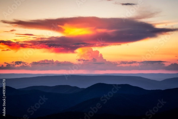 Fototapeta A anvil shaped cloud which is producing a small shaft of rain catches fire in the sunset light over the Blue Ridge Mountains.