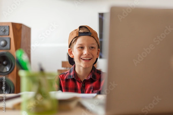 Fototapeta Happy elementary student having an online class at home.
