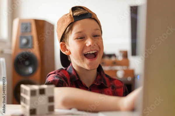 Fototapeta Happy elementary student talking to someone over video call at home.
