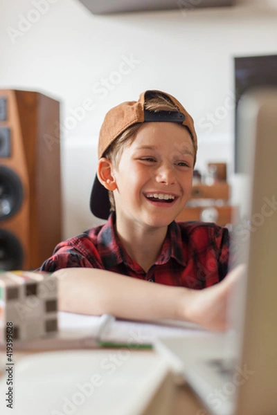 Fototapeta Happy elementary student talking during an online class over a computer at home.