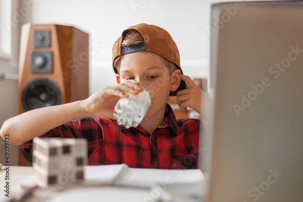 Fototapeta Elementary student drinking milk while learning at home.
