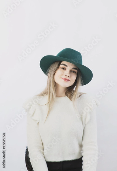 Fototapeta girl in a white sweater posing in a felt hat on a light background