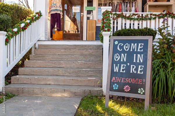 Fototapeta A sandwich board with a welcoming notice on it which reads : " Come on in, we are awesome " is placed in the front yard of a small local clothing shop in historic Clifton, Virginia.