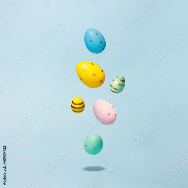 Fototapeta Colored easter decorated eggs flying on a blue background. Easter greeting card in minimalist style concept.Copy space