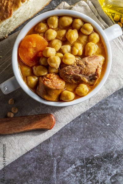 Fototapeta Chickpea stew dish (Madrid stew). With beef, chorizo, bacon, carrots and olive oil. Mediterranean diet. Homemade look. Top view with copy space.