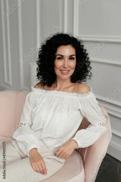 Obraz Woman in white blouse with african curls sits on sofa