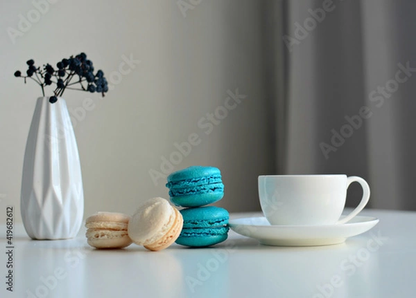 Fototapeta White cup of coffee, multicolored macaroons, vase with a sprig of dried berries on white background, close up