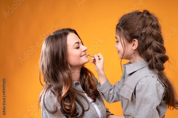 Obraz Beautiful woman sits with closed eyes while a little girl does her makeup while holding a brush in her hands
