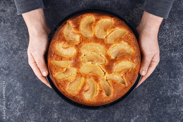 Obraz Man holding baked apple pie in hands on black background