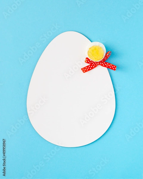 Fototapeta 2021 Easter unique composition made of white egg shape, peace of boiled egg and red ribbon. Vertical pastel blue background. Flat lay.