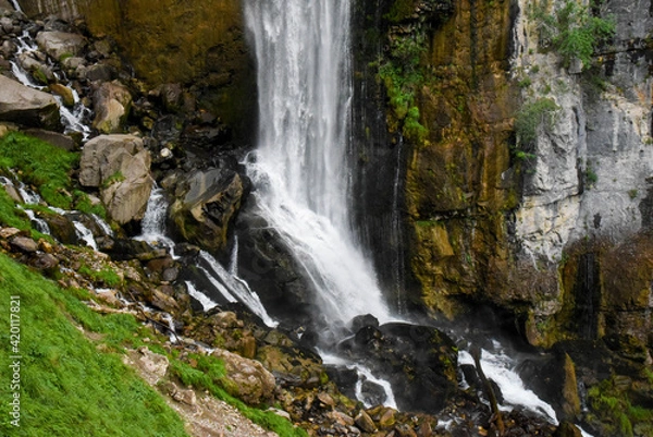 Fototapeta Beautiful waterfall in switzerland rushing down a cliff and bursting onto a steep rocky mountainside