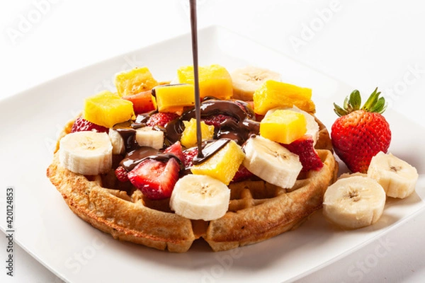 Fototapeta Waffle topped with strawberry, banana and orange fruits and dark chocolate