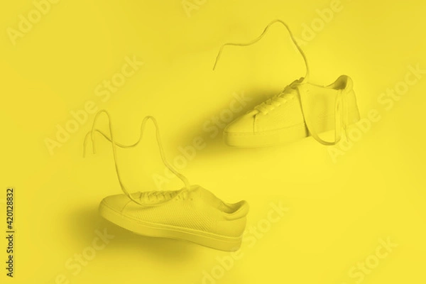 Fototapeta the concept of weightlessness and lightness. a pair of yellow sneakers flying in the air on a yellow background.