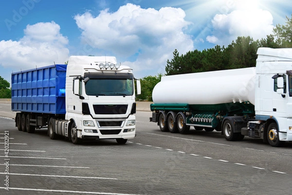 Fototapeta trucks is on a road - cargo transportation, shipping concept, blue container and white tanker truck, blank space on a side view