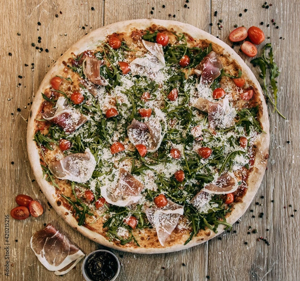 Fototapeta Pizza with bacon arugula and tomatoes. Top down view on delicious single round pizza with arugula lettuce and bacon meat toppings