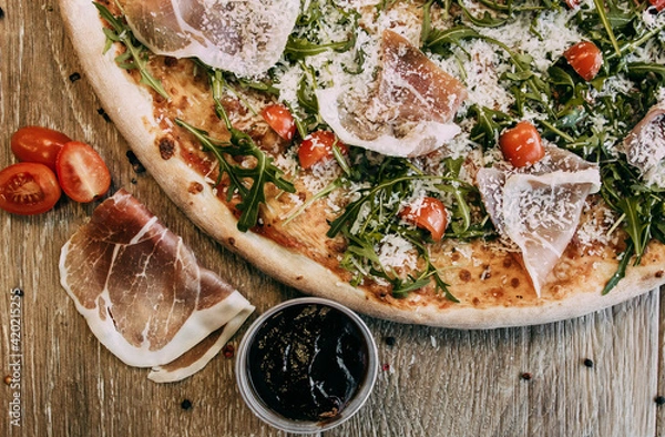 Fototapeta Pizza with bacon arugula and tomatoes. Top down view on delicious single round pizza with arugula lettuce and bacon meat toppings