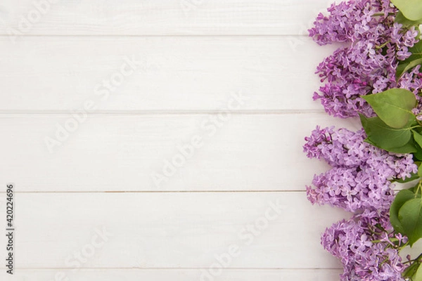 Obraz Top view of blooming lilac branches designed as one side frame on white wooden background. Copy space. Purple flowers flat lay