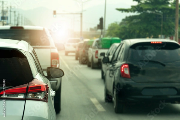 Fototapeta Transportation of white car on the road.  On the asphalt road. Queue with many cars and turn on the brake lights on the road to wait for the green traffic lights.