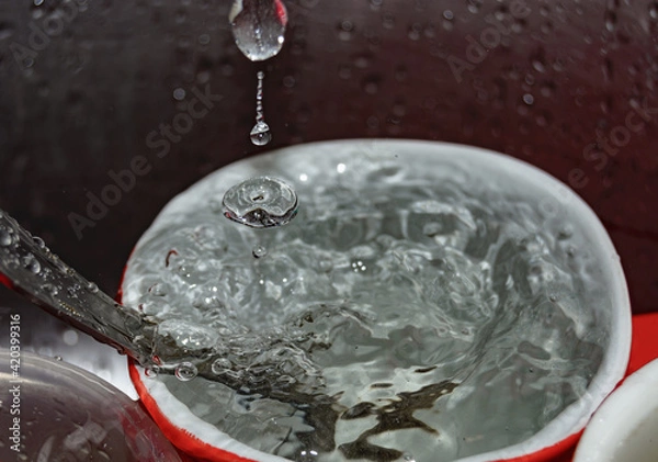 Fototapeta a stream of water pours into a mug with a spoon in the dish sink close-up. blurred focus