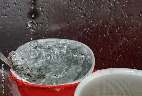 Fototapeta a stream of water pours into a mug with a spoon in the dish sink close-up. blurred focus