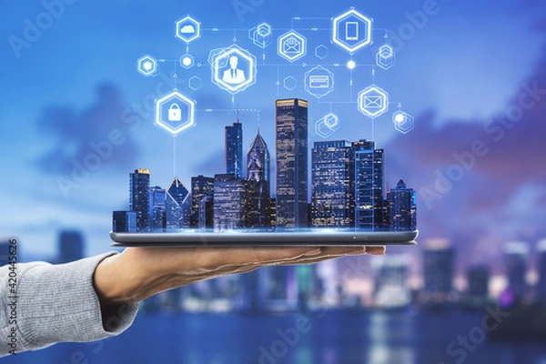 Fototapeta Cloud technology in smart city concept with human hand carries digital tablet with megapolis city skyscrapers and digital social network symbols above at skyline background