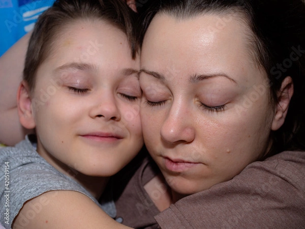 Obraz a young mother and son of 10 years old are sleeping in an embrace on the bed.