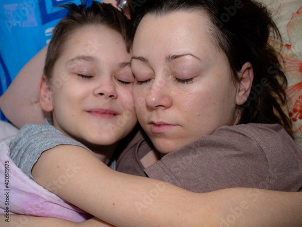 Obraz a young mother and son of 10 years old are sleeping in an embrace on the bed. a happy child.