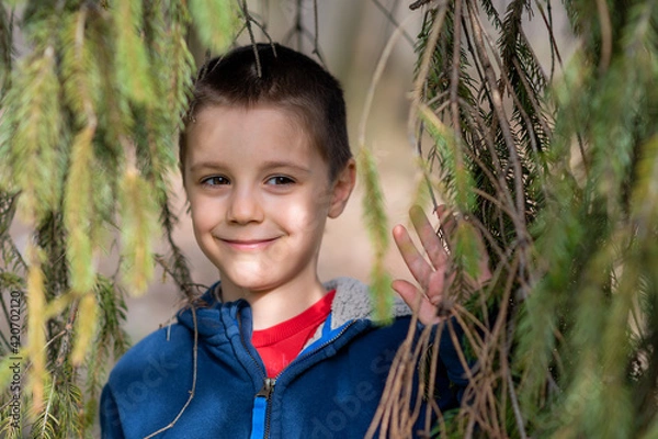 Obraz Portrait of little boy in nature. A boy peeks out from behind a branch