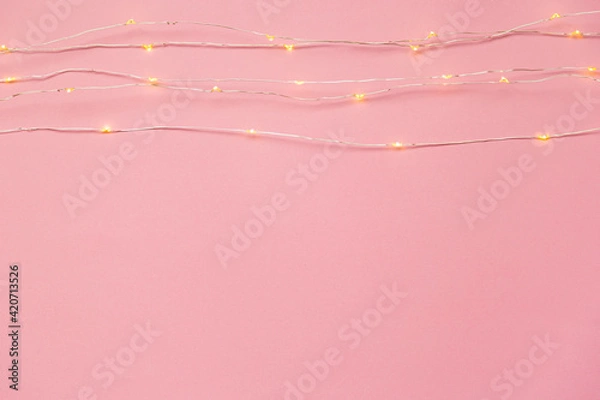 Fototapeta The garland is on. Glowing electric garland on a pink solid background. top view