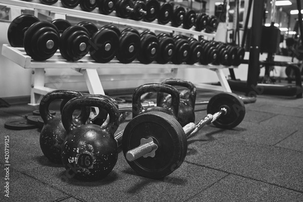 Fototapeta Dumbbells and kettlebells on a floor. Bodybuilding equipment. Fitness or bodybuilding concept background. black and white photography
